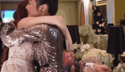 Woman In Sequined Jacket Hugging Woman In White Dress GIF