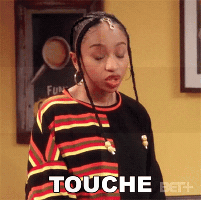 Woman In Striped Shirt Saying Touché In Front Of Yellow Wall GIF