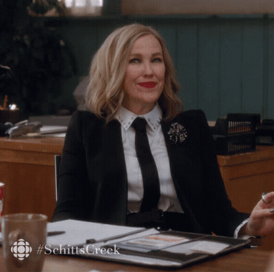 Woman In Suit And Tie At Desk With Hashtag Schitts Creek GIF
