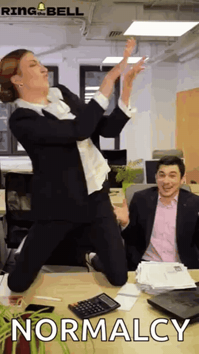 Woman In Suit Jumping In Front Of Man At Desk GIF