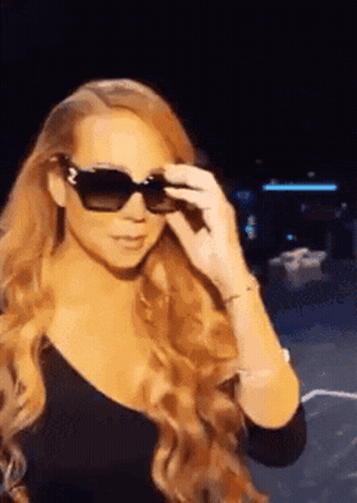 Woman In Sunglasses And Black Top Standing In Dark GIF