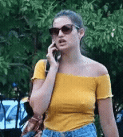Woman In Sunglasses And Yellow Off-Shoulder Top Talking On Phone GIF