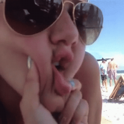 Woman In Sunglasses Licking Lips On Beach GIF