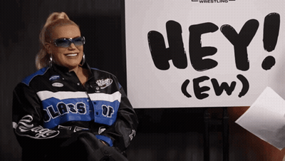 Woman In Sunglasses Smiling In Front Of Hey Sign GIF