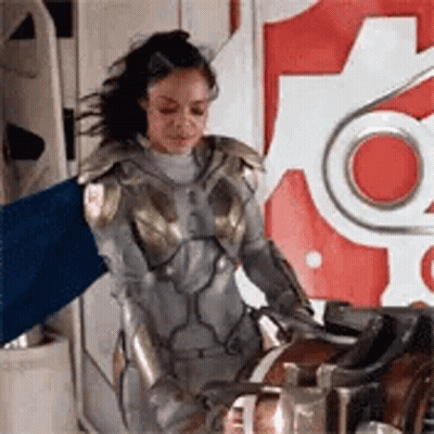 Woman In Superhero Costume Holding Blue Flag Next To Machine GIF