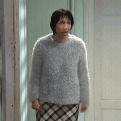 Woman In Sweater And Plaid Skirt Standing In Front Of Door GIF