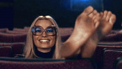 Woman In Theater With Feet Up Smiling GIF