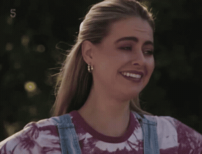 Woman In Tie Dye Shirt And Overalls Smiling With Number 5 GIF