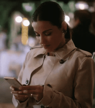 Woman In Trench Coat Looking At Phone GIF