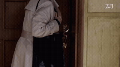 Woman In Trench Coat Standing In Front Of Door GIF