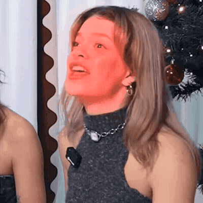Woman In Turtleneck And Earrings Smiling With Christmas Tree GIF