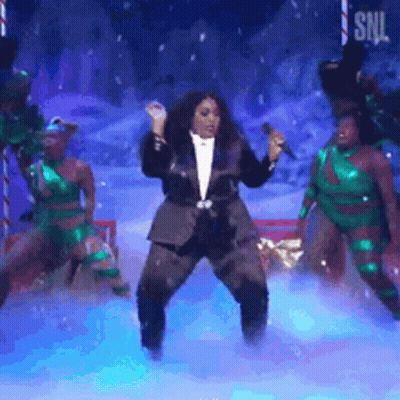 Woman In Tuxedo Singing Into Microphone Surrounded By Dancers GIF