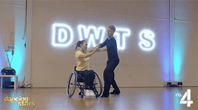Woman In Wheelchair Dancing With Man In Front Of DWTS Sign GIF
