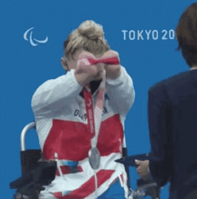 Woman in Wheelchair Holding Medal Against Blue Wall
