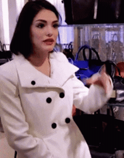 Woman In White Coat In Front Of Bags Display GIF