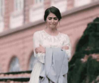 Woman In White Dress Holding Jacket In Front Of Building GIF