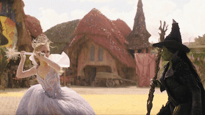 Woman In White Dress Holding Wand In Front Of Witch In Black Hat GIF