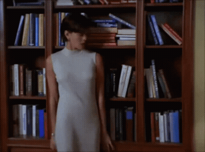 Woman In White Dress In Front Of Bookshelf With Bible GIF