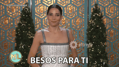 Woman In White Dress Says Besos Para Ti In Front Of Christmas Tree GIF