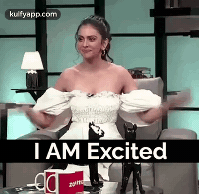 Woman In White Dress Sitting With Arms Outstretched Saying I Am Excited GIF