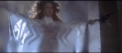 Woman In White Dress Standing In Front Of Door With Cloth Covering Her GIF