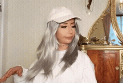 Woman In White Hat And Wig Standing Before Mirror GIF