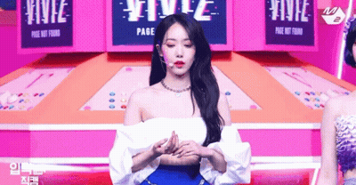 Woman In White Off-Shoulder Top And Blue Skirt On Stage With Microphone GIF