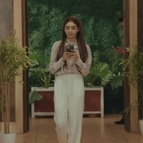 Woman In White Pants Looking At Phone While Walking GIF