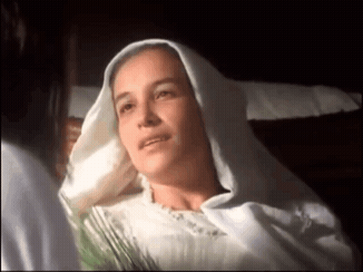 Woman In White Robe Laying In Bed Talking To Another Woman GIF