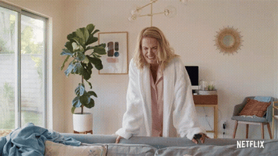 Woman In White Robe Standing Next To Couch With Netflix Logo GIF