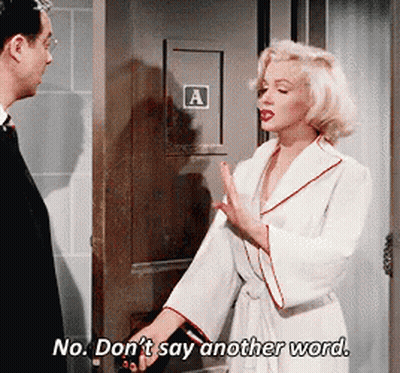 Woman In White Robe Talking To Man In Suit In Front Of Door With Letter A GIF