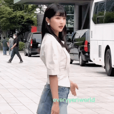 Woman In White Shirt And Blue Jeans Standing On Sidewalk GIF