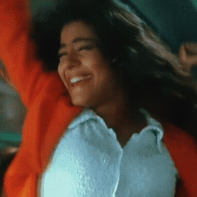 Woman In White Shirt And Orange Jacket Smiling With Arms Up GIF