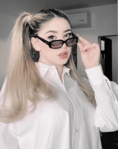 Woman In White Shirt And Sunglasses Looking At Camera GIF