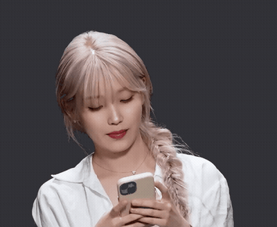 Woman In White Shirt Holding Phone With Braided Ponytail GIF