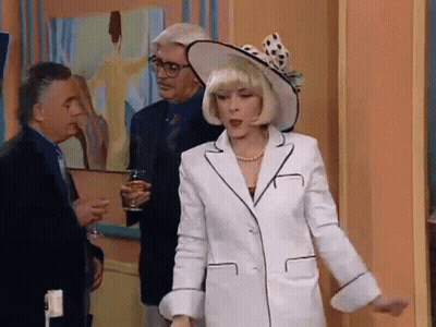 Woman In White Suit And Hat Standing Before Two Men GIF
