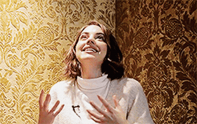 Woman In White Sweater In Front Of Gold Pattern Wall GIF