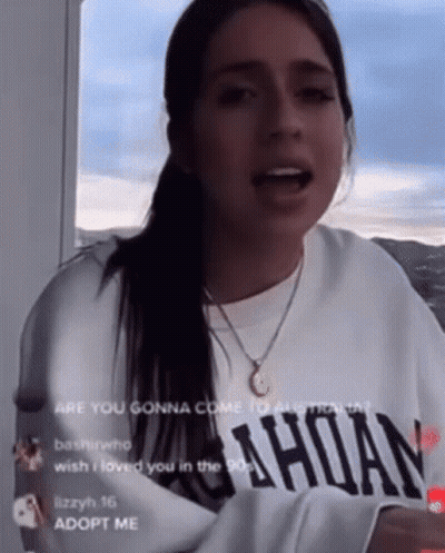 Woman In White Sweatshirt And Gold Necklace Talking On Balcony GIF