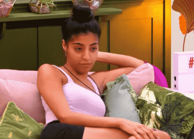 Woman In White Tank Top Sitting On Couch With Pillows GIF