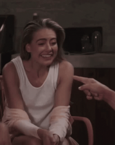 Woman In White Tank Top Sitting With Hand Pointing At Her GIF