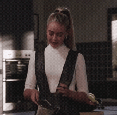 Woman In White Turtleneck And Black Overalls In Kitchen GIF