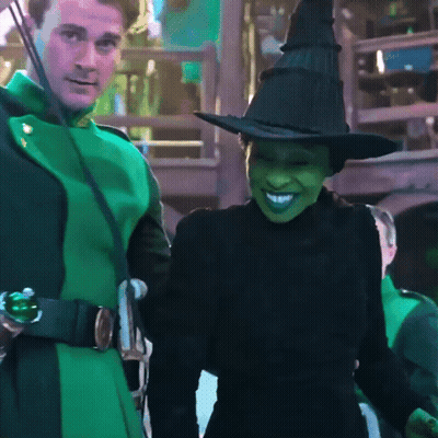 Woman In Witch Costume Smiling Next To Man In Green Coat GIF