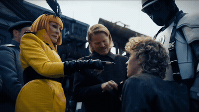 Woman In Yellow Coat Pointing At Man In Black Suit GIF