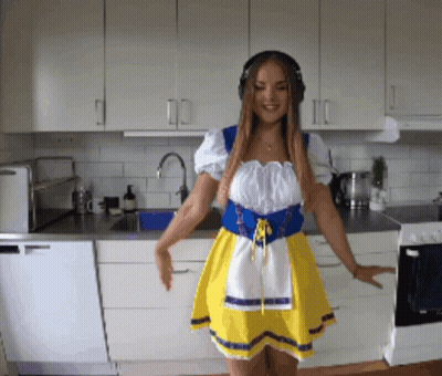 Woman In Yellow Dress Dancing With Headphones In Kitchen GIF