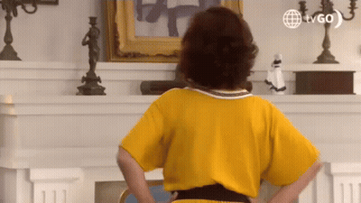 Woman In Yellow Dress Hands On Hips By Fireplace GIF