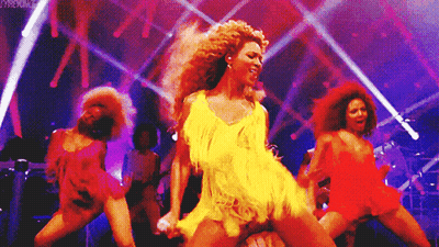 Woman In Yellow Dress Singing Into Microphone Surrounded By Dancers GIF