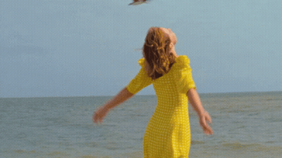 Woman In Yellow Dress With Arms Outstretched By Ocean GIF
