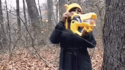 Woman In Yellow Hat Holding Toy Gun In Woods GIF