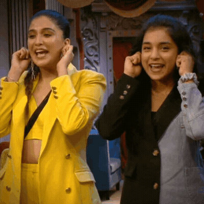Woman In Yellow Jacket Adjusting Earring Next To Woman In Black Jacket GIF
