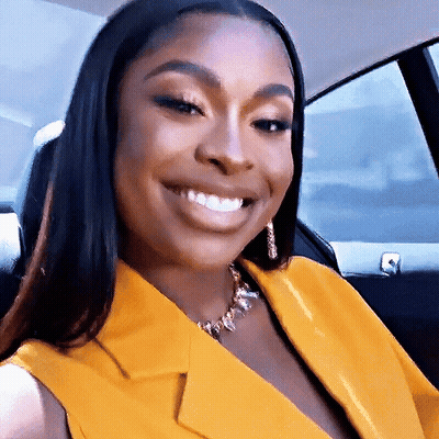 Woman In Yellow Jacket And Gold Necklace Smiling In Car GIF